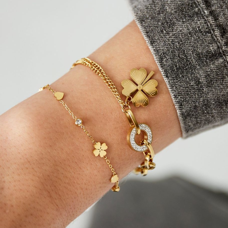 image Goldenes Ella Lou Armband mit Herz-, Stern- und Kleeblattanhängern am Handgelenk kombiniert mit weiteren Schmuckstücken