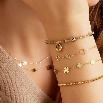 Goldenes Joyful Lou Armband mit Symbolen (Herz, Stern, Kleeblatt) am Handgelenk einer Frau im Layering-Look – Ankerliebe Schmuck