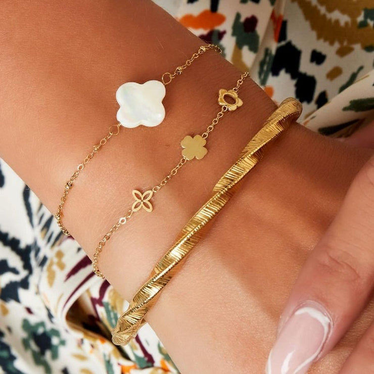 Nahaufnahme eines Handgelenks mit drei Armbändern, darunter das Mira Lou Armband aus goldfarbenem Edelstahl mit floralen Motiven