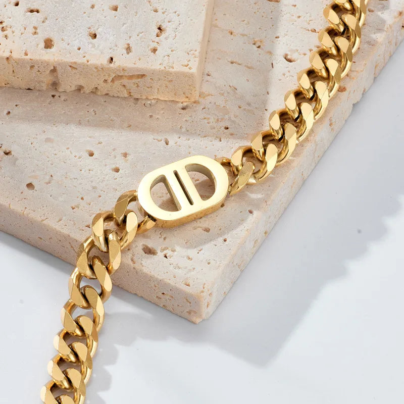 Goldene Edelstahl-Halskette mit Gliederkette und markantem Mittelstück im minimalistischen Design, fotografiert auf beigem Naturstein