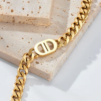 Goldene Edelstahl-Halskette mit Gliederkette und markantem Mittelstück im minimalistischen Design, fotografiert auf beigem Naturstein
