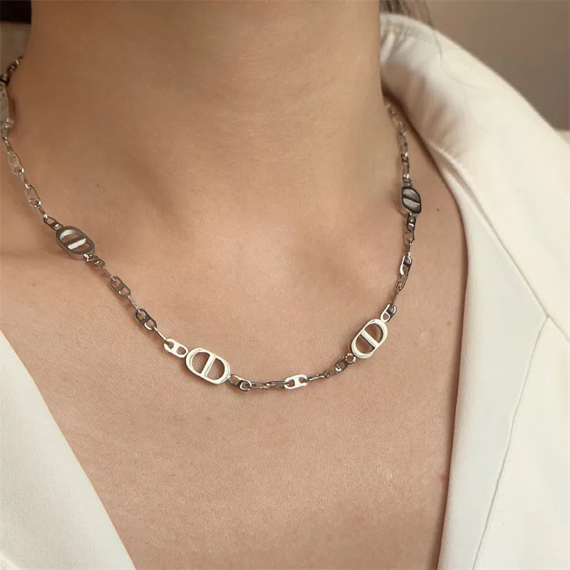 Silberne Edelstahl-Gliederkette mit ovalen Elementen, getragen von einer Frau mit weißem Oberteil