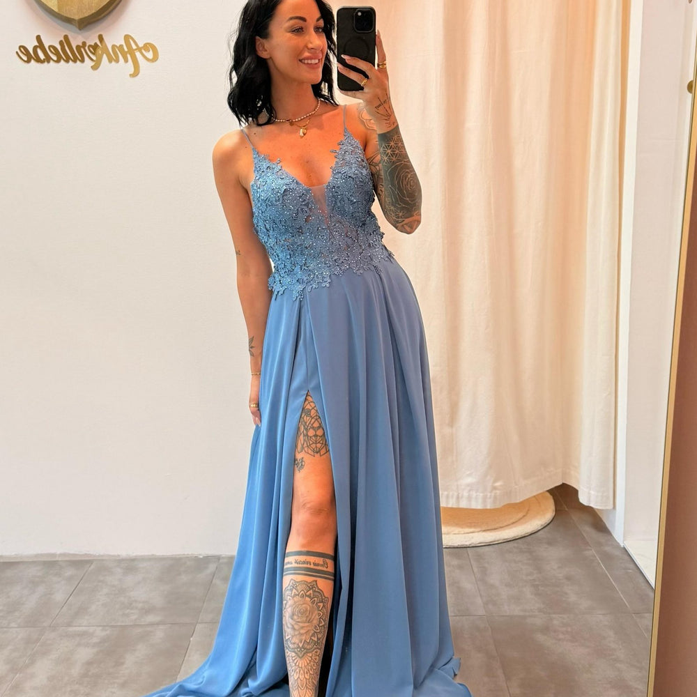 Model trägt das staubblaue Abendkleid „Lyanna“ mit floraler Spitze, Schlitz und zarten Trägern – ein femininer Look für besondere Anlässe.