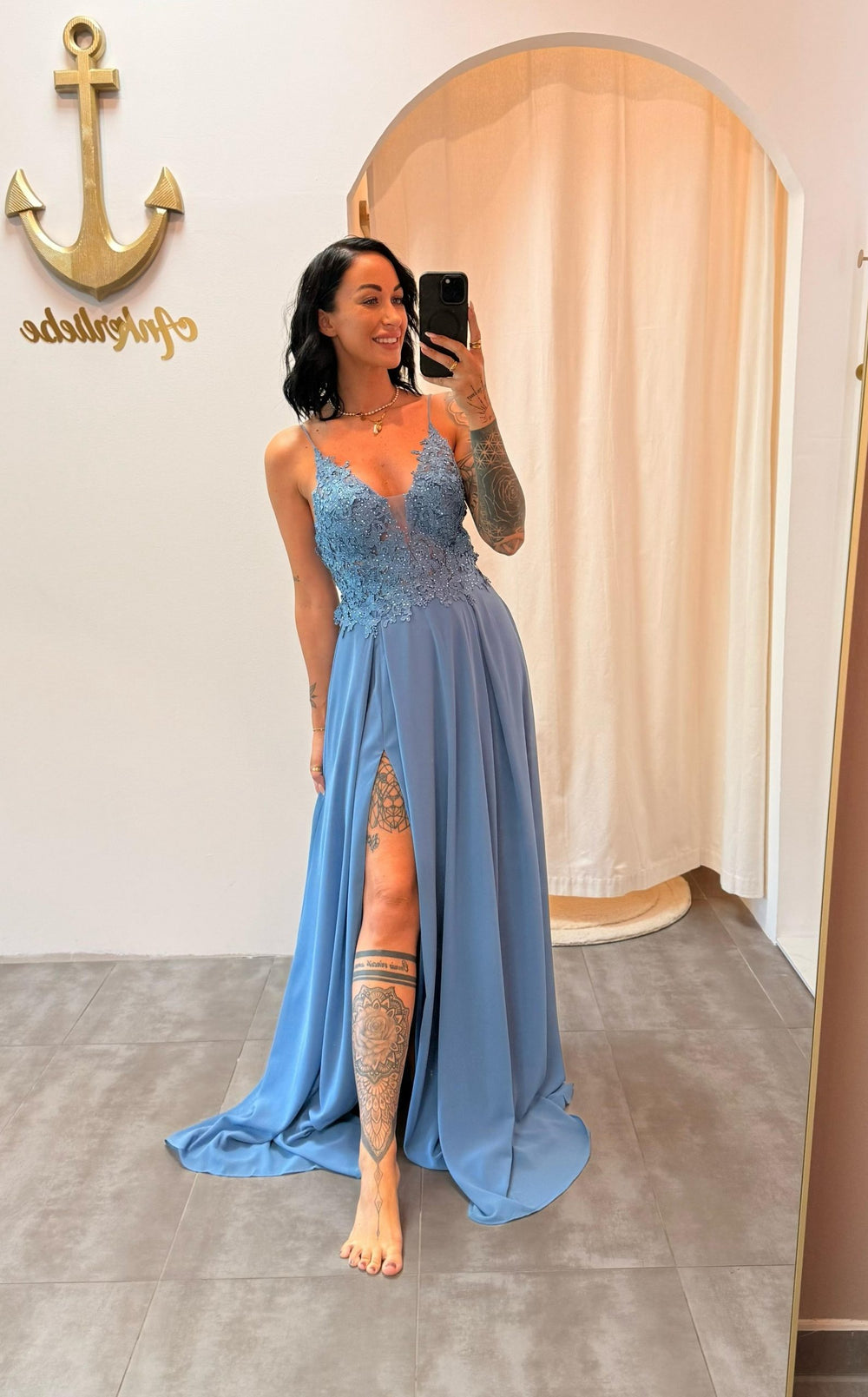 Model trägt das staubblaue Abendkleid „Lyanna“ mit floraler Spitze, Schlitz und zarten Trägern – ein femininer Look für besondere Anlässe.