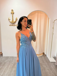 Model trägt das staubblaue Abendkleid „Lyanna“ mit floraler Spitze, Schlitz und zarten Trägern – ein femininer Look für besondere Anlässe.