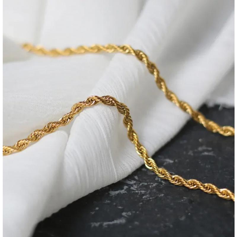 Gedrehte goldene Edelstahlkette im Rope Chain Design auf weißem Stoff fotografiert