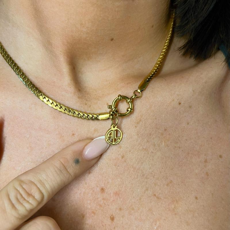 image Goldene Kette aus Edelstahl mit rundem AL-Anhänger und Karabinerverschluss am Hals einer Frau