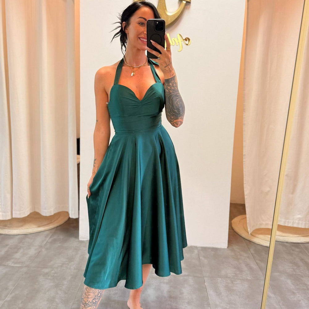 Frau trägt ein smaragdgrünes Satin-Midikleid mit Neckholder, schwingendem Rock und Taschen – fotografiert im Ankerliebe-Store.